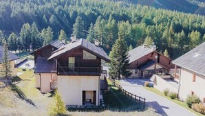 A mountain lodge with multiple wooden cabins, a covered outdoor seating area, and a view of a forested valley.