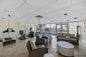 Un gimnasio con equipamiento de ejercicio, una cinta de correr y una zona de descanso con un sofá y un reposapiés.