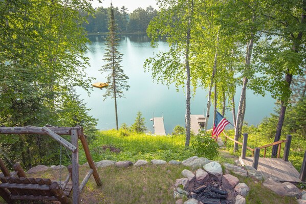 A lakeside cabin with a deck, a fire pit, and an American flag. - Cozy Stone Cottage overlooking Smith Lake (Marcell)