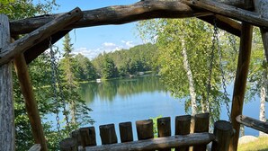 A wooden bench under a rustic wooden structure overlooking a lake surrounded by trees. - Cozy Stone Cottage overlooking Smith Lake (Marcell)