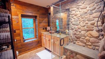 Une salle de bain avec un mur en pierre, des meubles en bois, une douche en verre et une fenêtre.