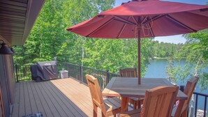 A wooden deck with a table and chairs, a red umbrella, and a grill. - Cozy Stone Cottage overlooking Smith Lake (Marcell)