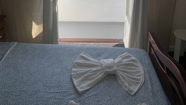 A room with a bed, a window with curtains, and a view of buildings outside. - Liberdade direito - Hostel (Braga)