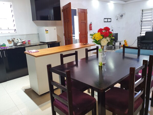 A modern kitchen with a central island, wooden dining table with chairs, and a vase with flowers. - Apartment for Family (Suva)