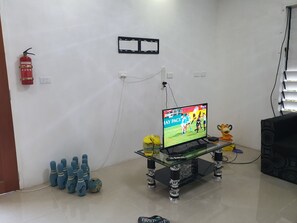 A room with a television on a glass table, a fire extinguisher, a bowling set, and a toy lion. - Apartment for Family (Suva)
