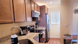 A kitchen with granite countertops, stainless steel appliances, wooden cabinets, and a window with blinds.