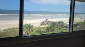A beach view from a window with a wooden deck and palm trees.