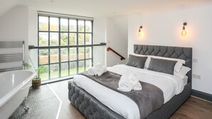 Une chambre moderne avec une grande fenêtre, une baignoire et un lit agrémenté de serviettes roulées.