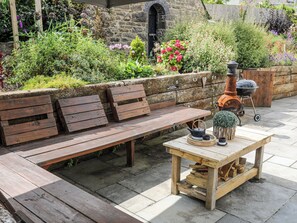 An outdoor seating area with wooden benches and a table with a kettle and cups.