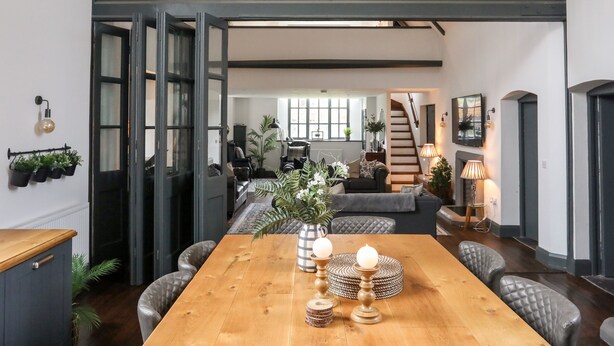 Un vaste espace dédié à la salle à manger, avec une table en bois, des chaises rembourrées et une vue sur un escalier menant à l’étage supérieur.