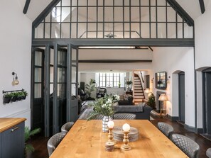 A spacious dining area with a wooden table, cushioned chairs, and a view of a staircase leading to an upper level.