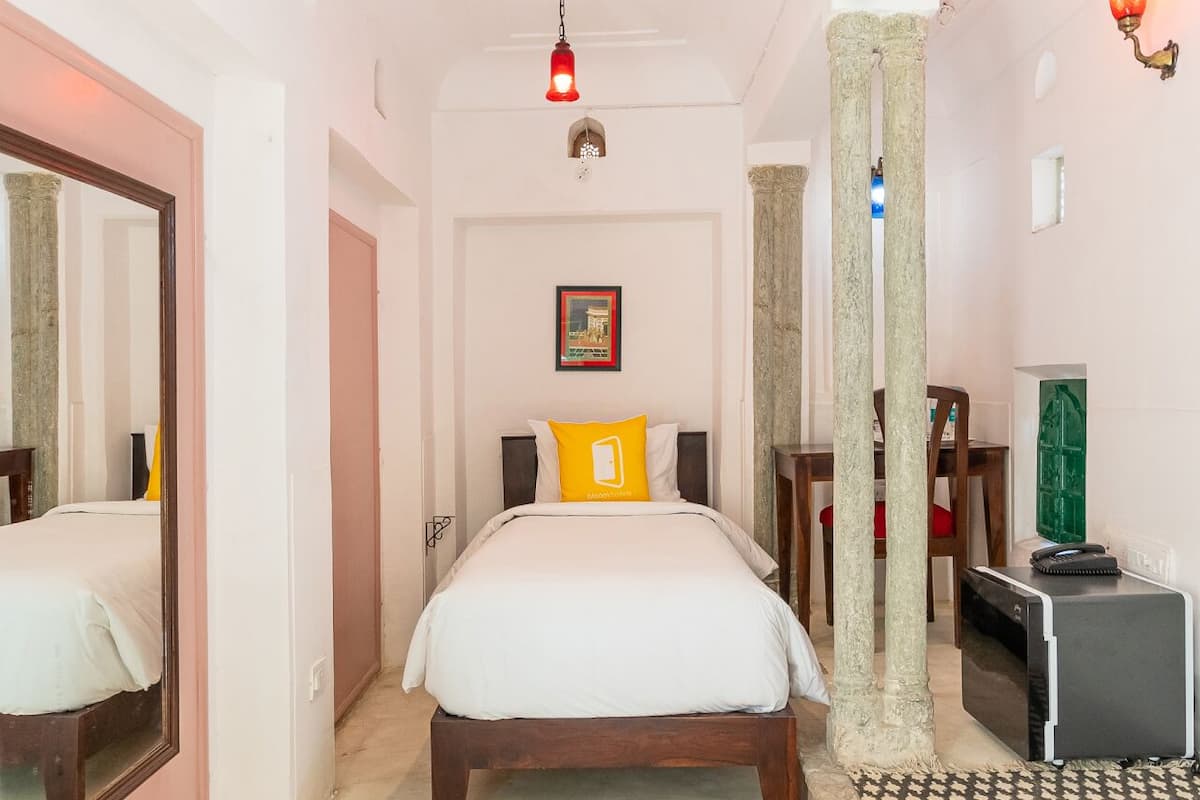 Quarto de hotel com uma cama, um espelho, uma escrivaninha e uma cadeira.