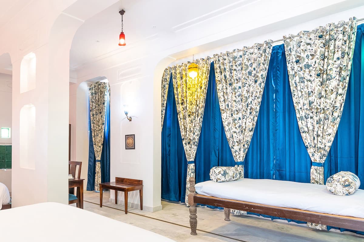 Quarto com cama, uma cadeira de madeira, um banco e um tapete estampado.