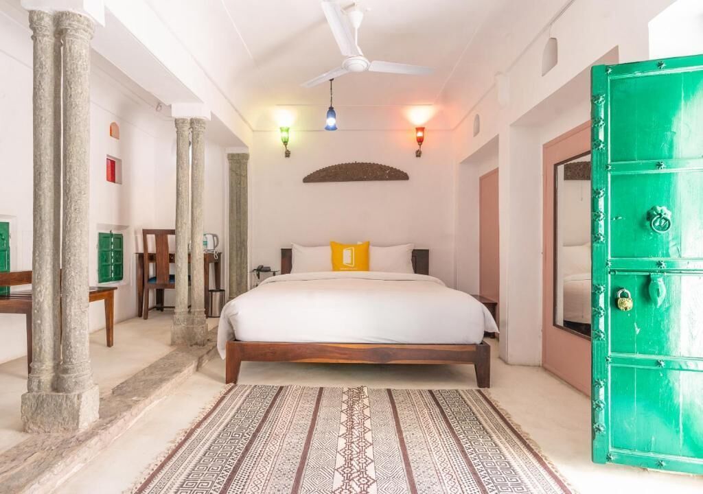 Un dormitorio con cama, una puerta verde, ventilador de techo y alfombra estampada.