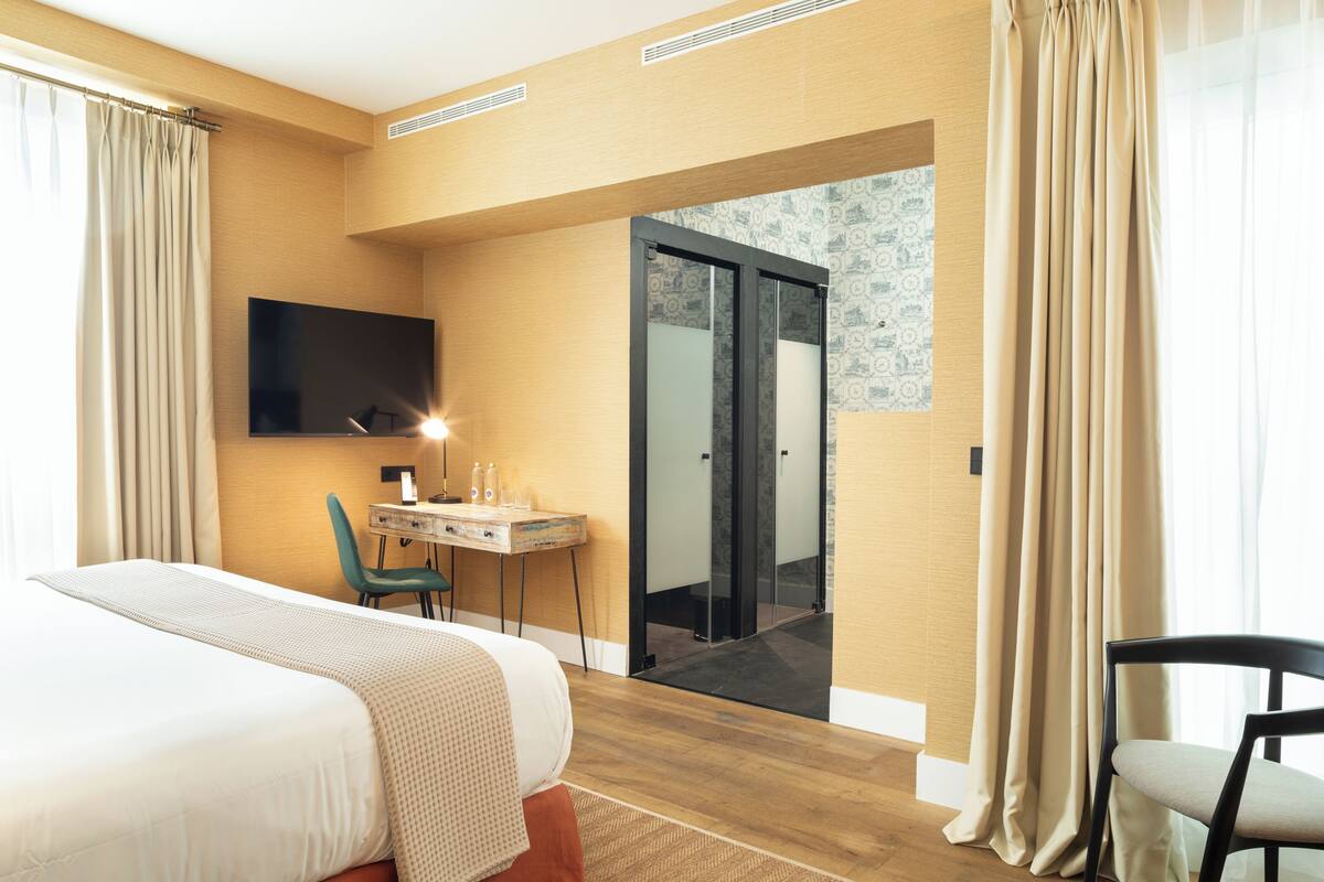 Hotellihuone, jossa on sänky, työpöytä, tuoli, televisio ja parveke, jossa on verhot.