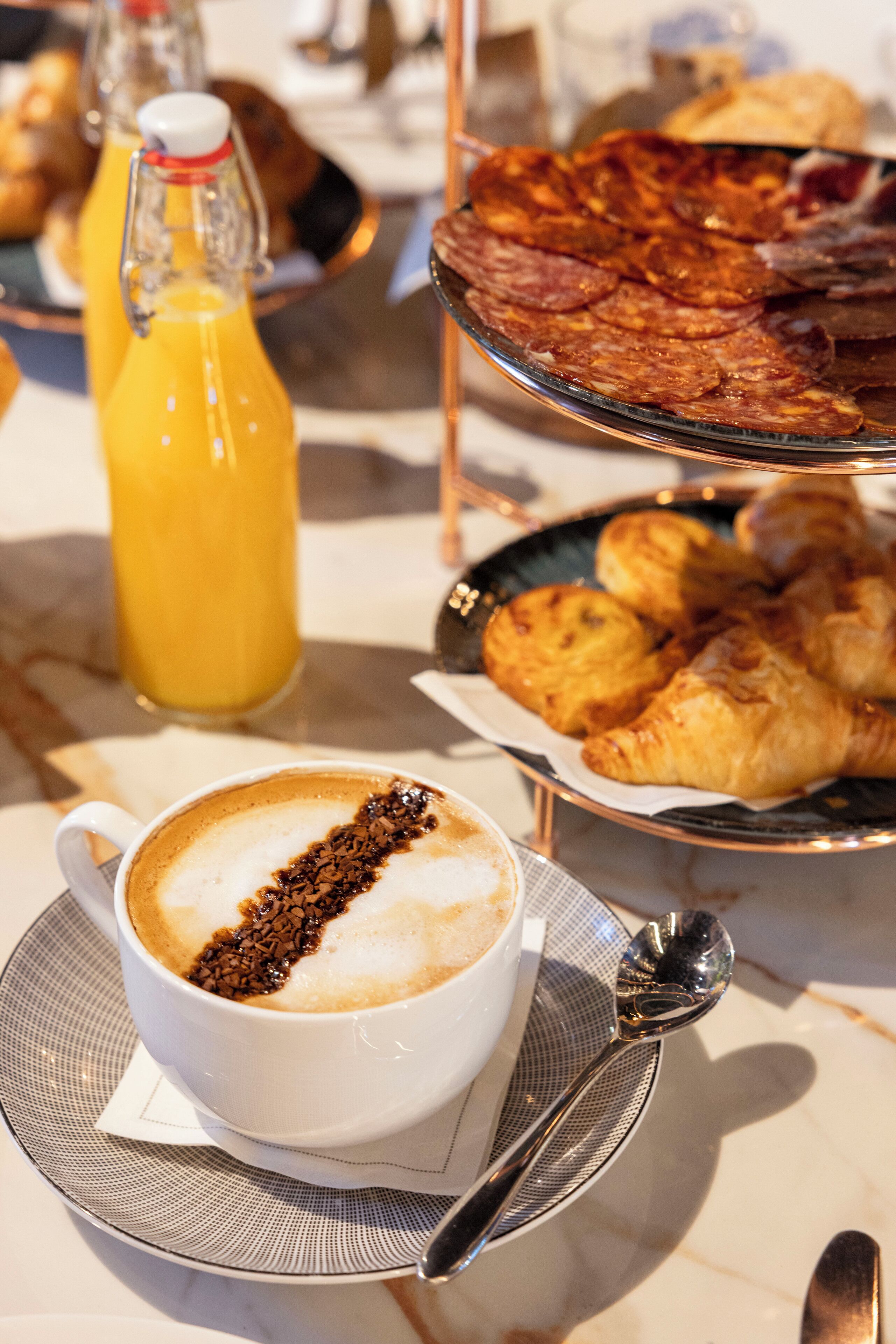 A breakfast setting with a cup of coffee, croissants, and a bottle of orange juice on a table.