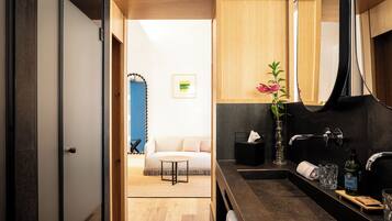 A modern bathroom with a dark countertop, a mirror, a sink, and a vase with a plant.