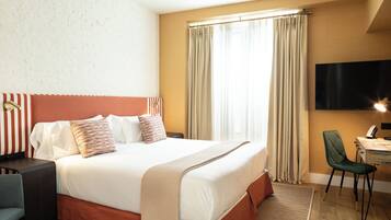 Ein Hotelzimmer mit einem großen Bett, einem Schreibtisch mit Stuhl, einem Fernseher und Vorhängen am Fenster.
