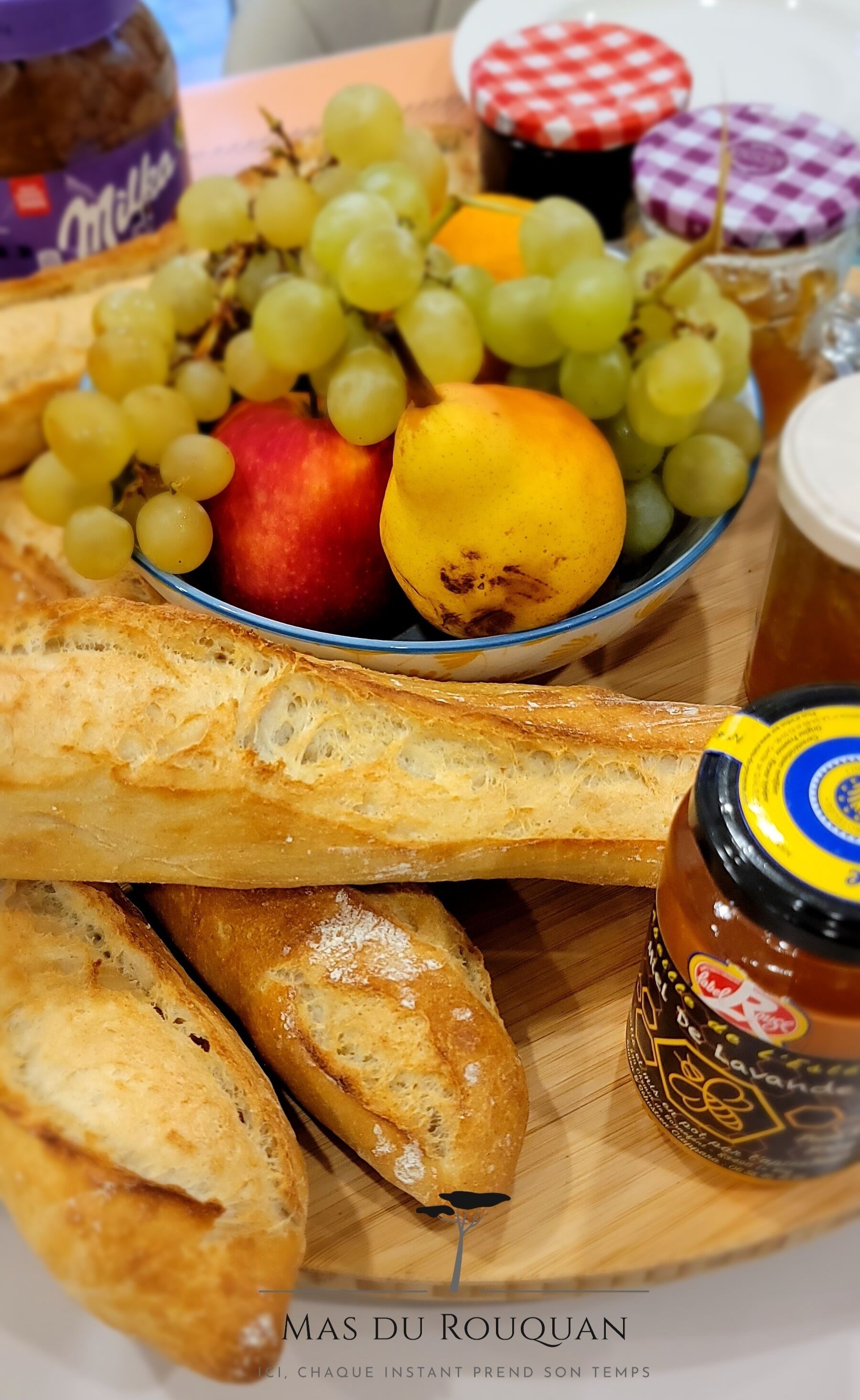 Ein Holzbord mit einer Schüssel Früchten, Baguettes und Gläsern mit Marmelade.
