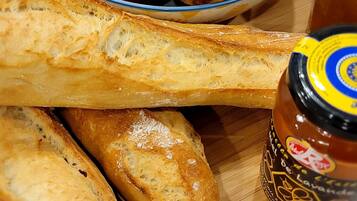 Ein Holzbord mit einer Schüssel Früchten, Baguettes und Gläsern mit Marmelade.