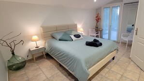 A bedroom with a bed, bedside tables, a lamp, a vase, and a view of the outside through a sliding door. - le Mas du Rouquan (Vidauban)