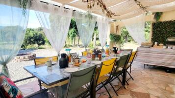 Un espace extérieur aménagé pour les repas, avec une table dressée pour quatre personnes, entourée de chaises, et un barbecue à l’arrière-plan.