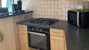 Une cuisine compacte équipée d’une cuisinière à gaz, d’un four, d’un four à micro-ondes et d’une hotte noire.