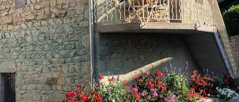A stone building with a balcony and flower beds.