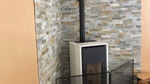 Une pièce avec un mur décoré d’un motif en pierre, une cheminée avec un conduit noir et un espace salon fermé par des parois de verre.