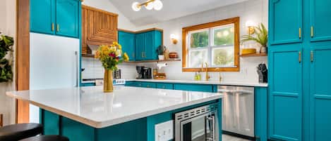 Una cocina con gabinetes color turquesa, encimera blanca y horno empotrado.