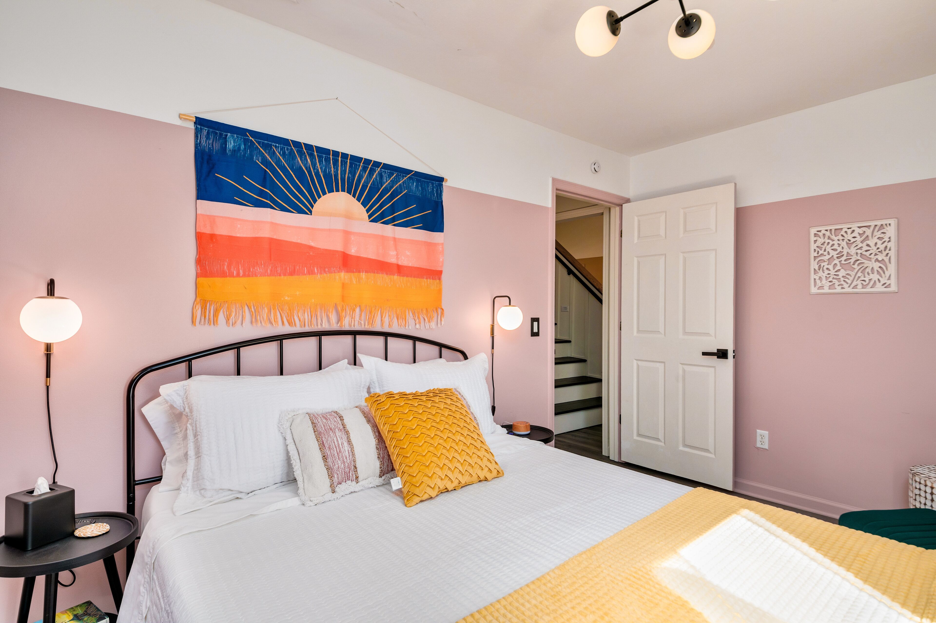 Un dormitorio con cama, lámparas de noche, un tapiz en la pared y una escalera.