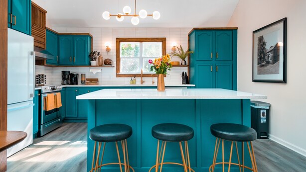 Une cuisine moderne avec des meubles de couleur turquoise, un îlot central blanc doté de tabourets et une grande fenêtre.