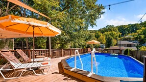 Une terrasse en bois avec une piscine, des chaises longues et des parasols.