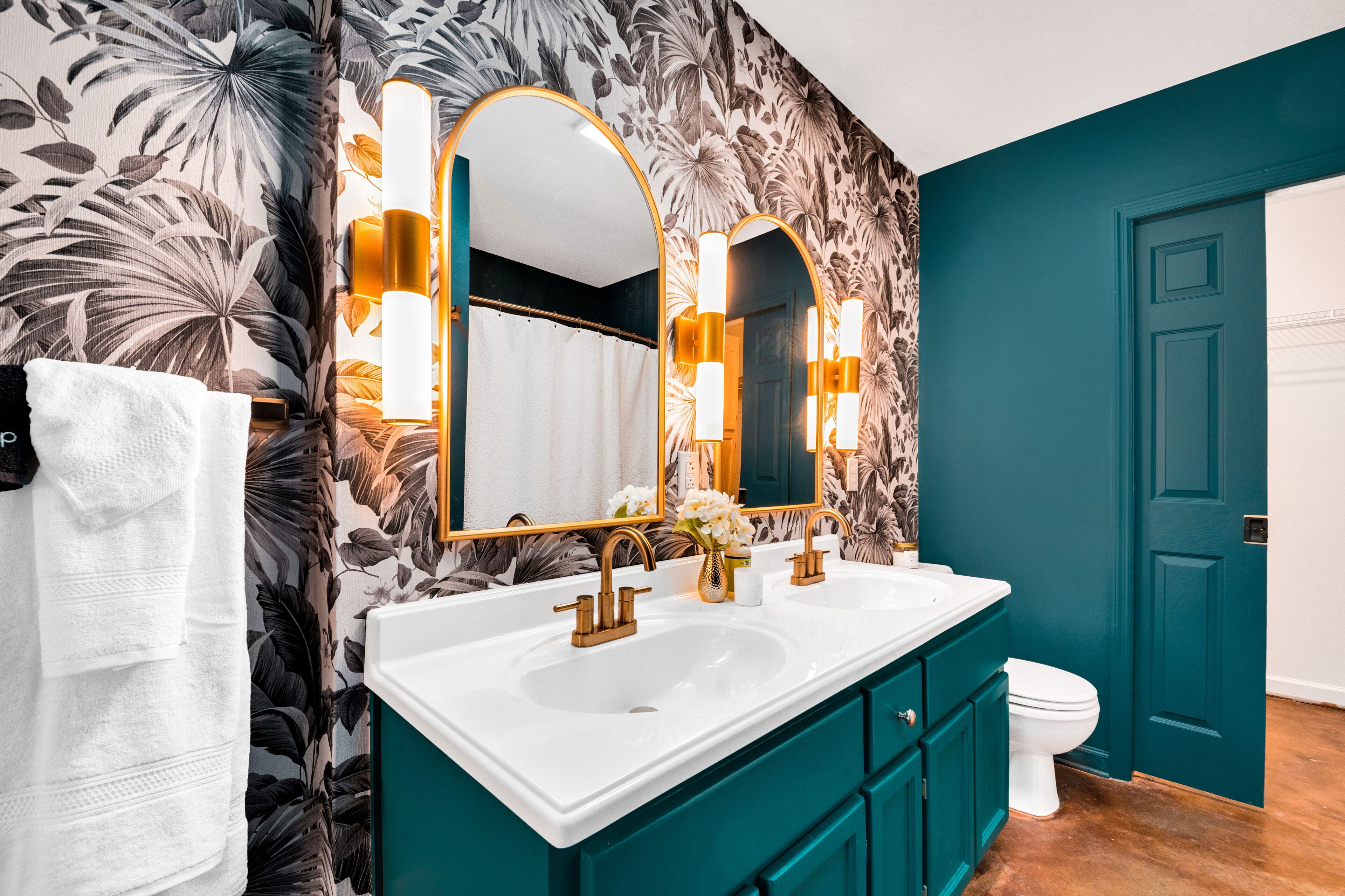A bathroom with a white sink, two gold faucets, and a mirror with gold sconces.