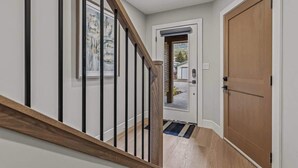 A hallway with a wooden staircase, a door, and a framed picture on the wall. - BRAND NEW|Hofburg by SSR|TopView|Luxury|PRIVATE HOT TUB|4BR plus Den ( BL# RES-11683 ) (Canmore)