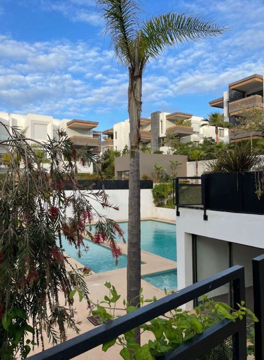 A modern hotel with a pool, surrounded by palm trees and other greenery.