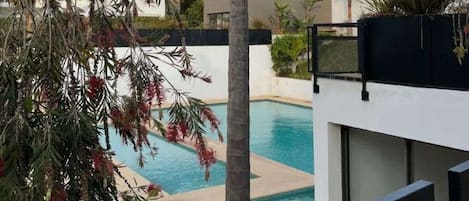A modern residential area with a swimming pool, palm trees, and contemporary houses.