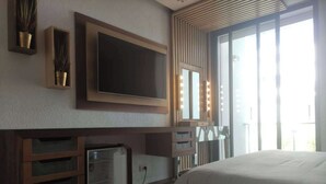 Ein Schlafzimmer mit einem großen Bett, einem an der Wand montierten Fernseher, einem Schminktisch mit Spiegel und Beleuchtung sowie einem kleinen Kühlschrank.