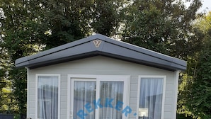 Een laag, enkelvoudig gebouw met een grijs dak en witte muren, met een houten terras ervoor.