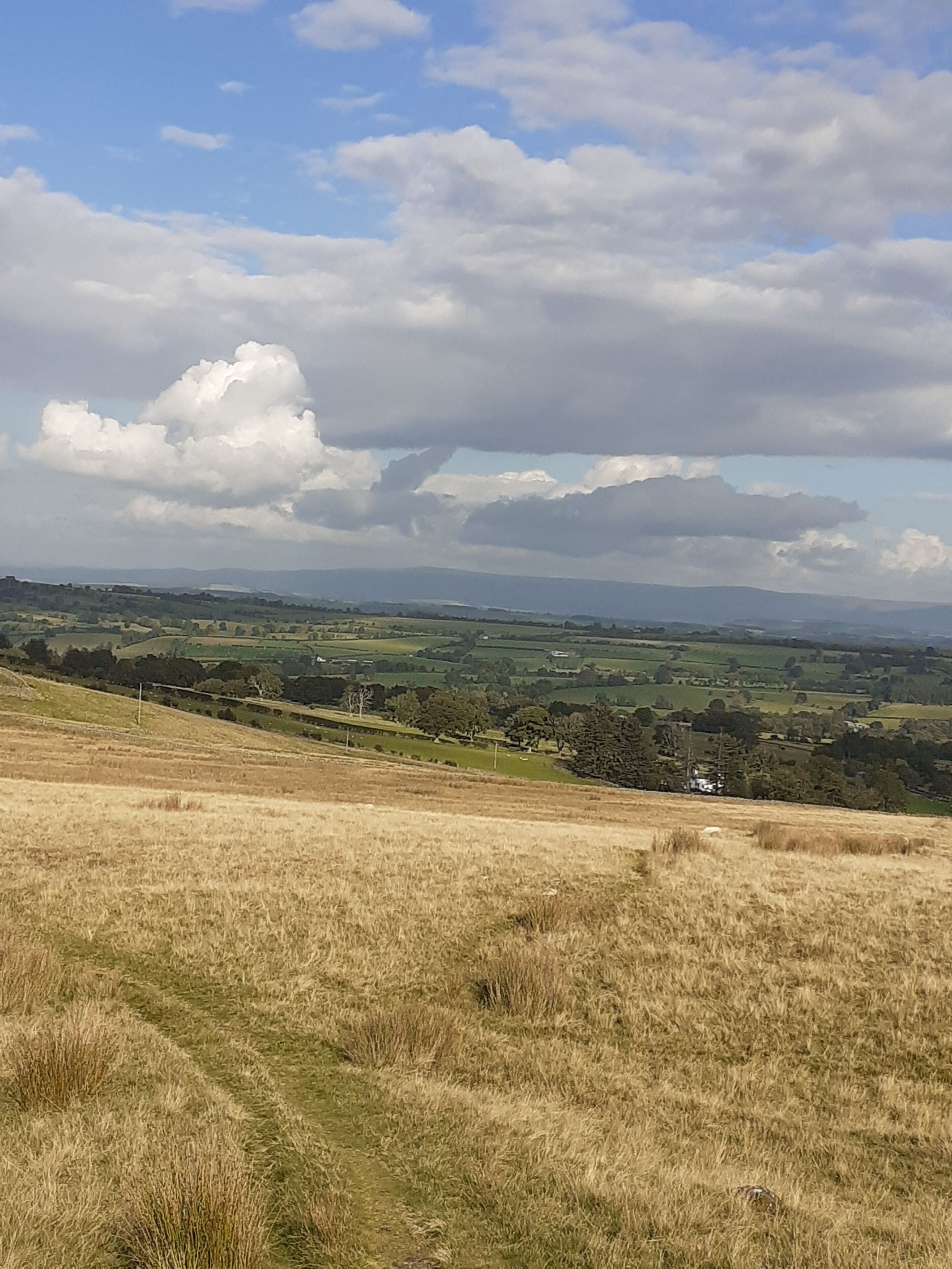 Vista panorámica de un paisaje montañoso con campos, colinas distantes y un cielo parcialmente nublado.