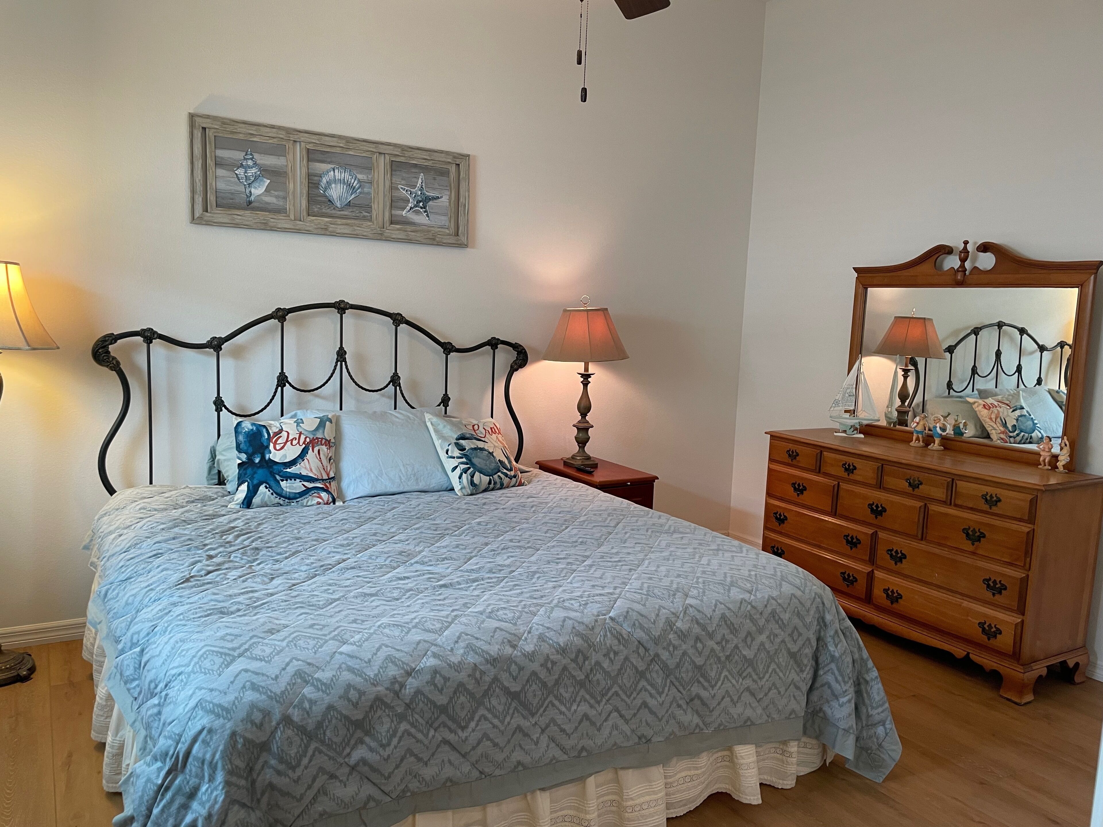 A bedroom with a bed, a dresser, a nightstand, a lamp, and a wall-mounted mirror.