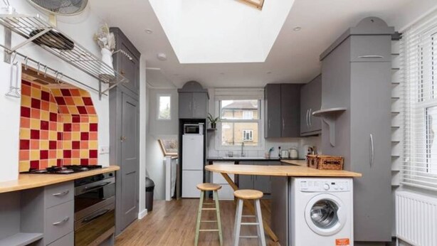 A compact kitchen with a built-in washing machine, a microwave, and a small dining area with stools. - Homely 1 Bedroom Apartment in Fulham! (London)