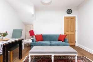A living room with a blue sofa, red cushions, a white bench, a small table with a lamp, and a patterned rug.