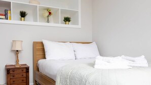 A neatly made bed with white linens, a wooden headboard, and a bedside table with a lamp. - Homely 1 Bedroom Apartment in Fulham! (London)