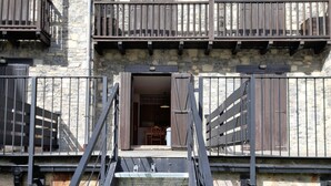 A stone building with a wooden balcony, metal stairs, and a door leading to an interior space.