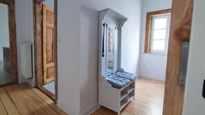 A room with wooden flooring, a white bench with storage, a door, and a window.
