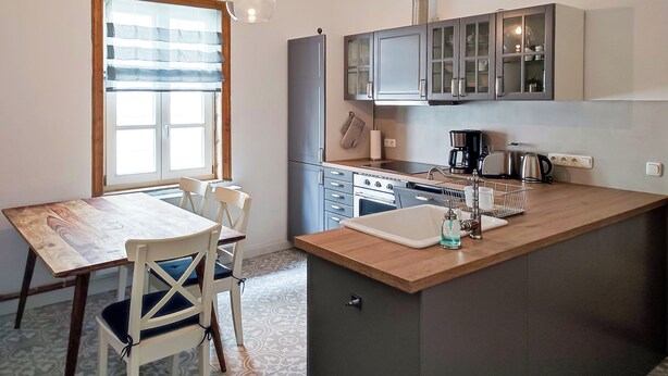 A compact kitchen with a wooden table and chairs, a built-in oven, and a sink.
