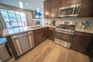Enjoy cooking in this well-equipped kitchen with a microwave, oven, and dishwasher, complemented by dark cabinetry and a view of the surrounding landscape.