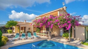 Zona piscina con piscina, sedie a sdraio e un edificio ricoperto di viti fiorite rosa.
