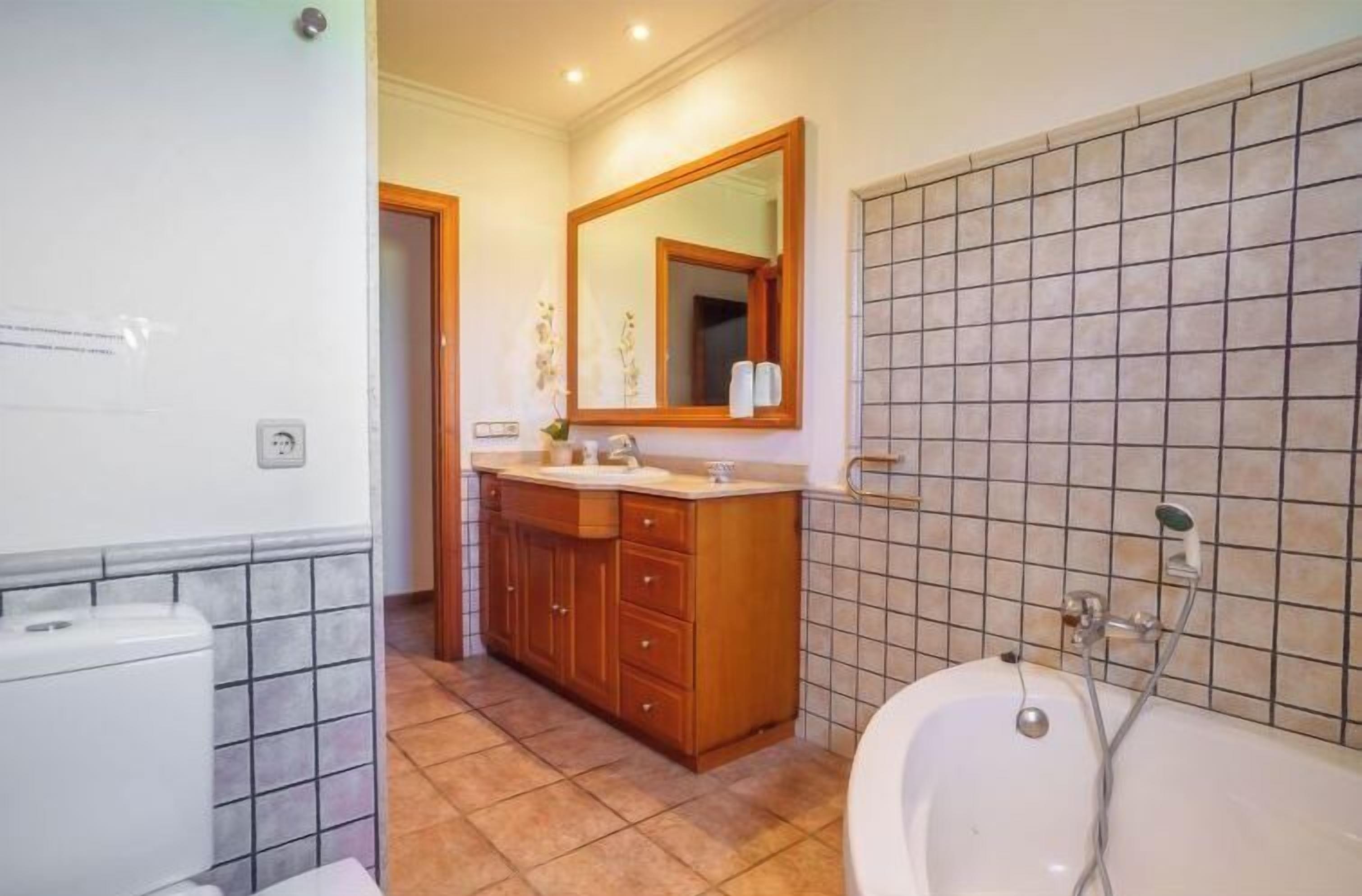 A bathroom with a toilet, sink, vanity, mirror, and bathtub.